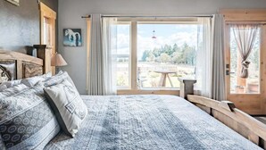 A bedroom with a large bed, a view of the outdoors, and a wooden bench by the window. - Roosters Coop - Wine Country at a Rustic, Lodge Style Retreat with Hot Tub & Pool (Newberg)