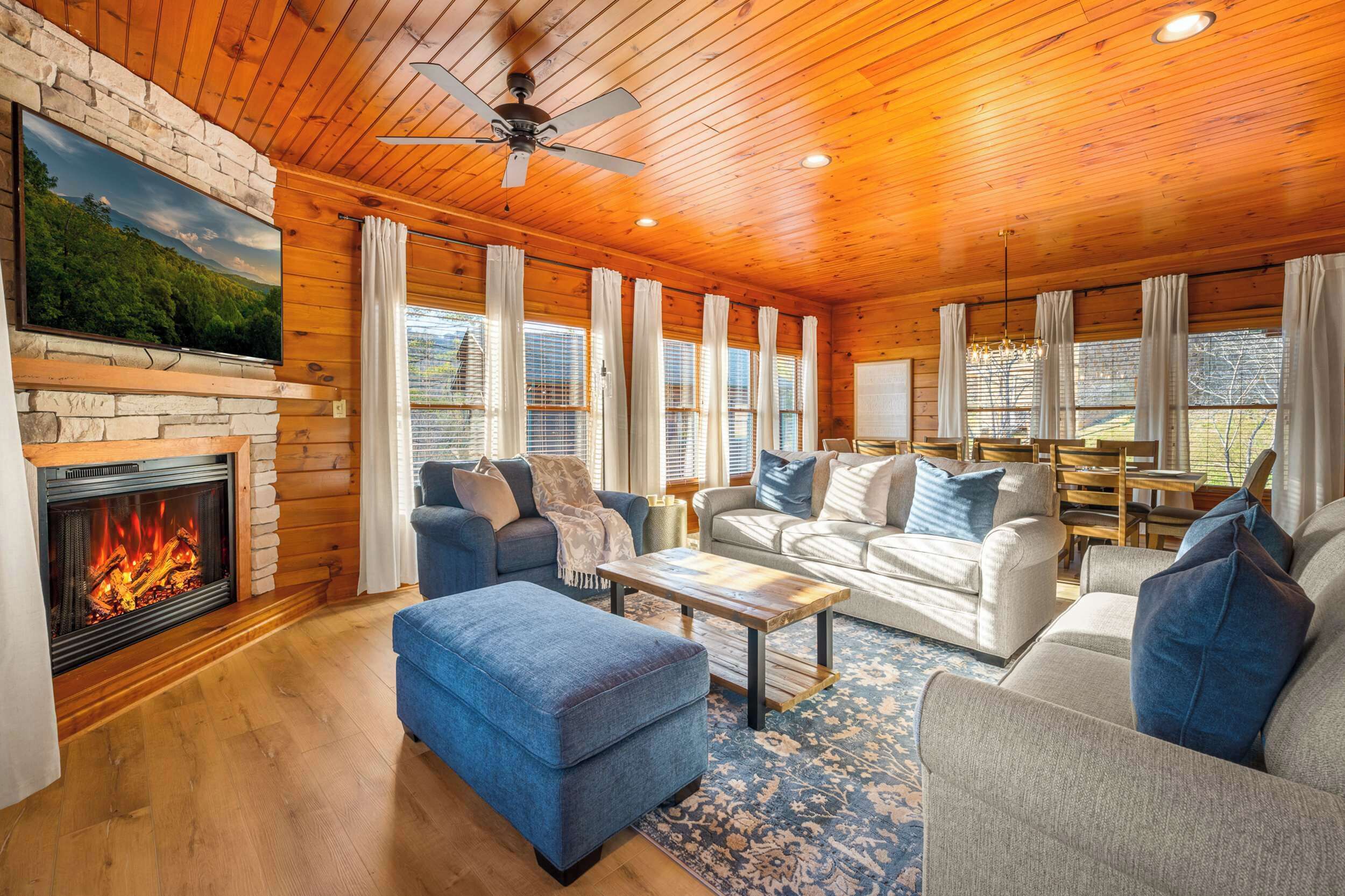 A cozy living room with a fireplace, wooden ceiling, and large windows.