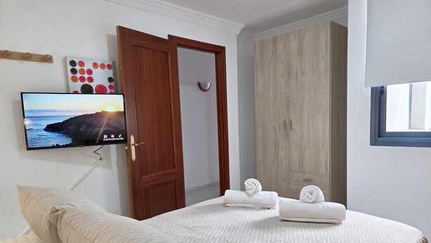 A bedroom with a bed, a TV mounted on the wall, a wooden wardrobe, and a window. - Naos Costa Atlantica - Puerto Naos (Puerto Naos)