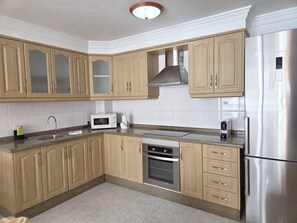 A kitchen with wooden cabinets, a stainless steel refrigerator, a microwave, and an oven.