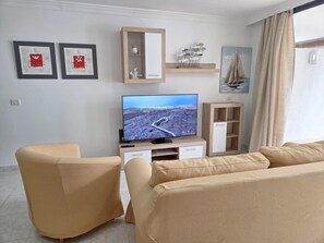 A living room with a TV, two framed artworks, a wooden cabinet, and a sailboat painting.