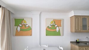 A small dining area with a white table and chairs, two paintings on the wall, and a kitchen area with wooden cabinets. - Naos Costa Atlantica - Puerto Naos (Puerto Naos)