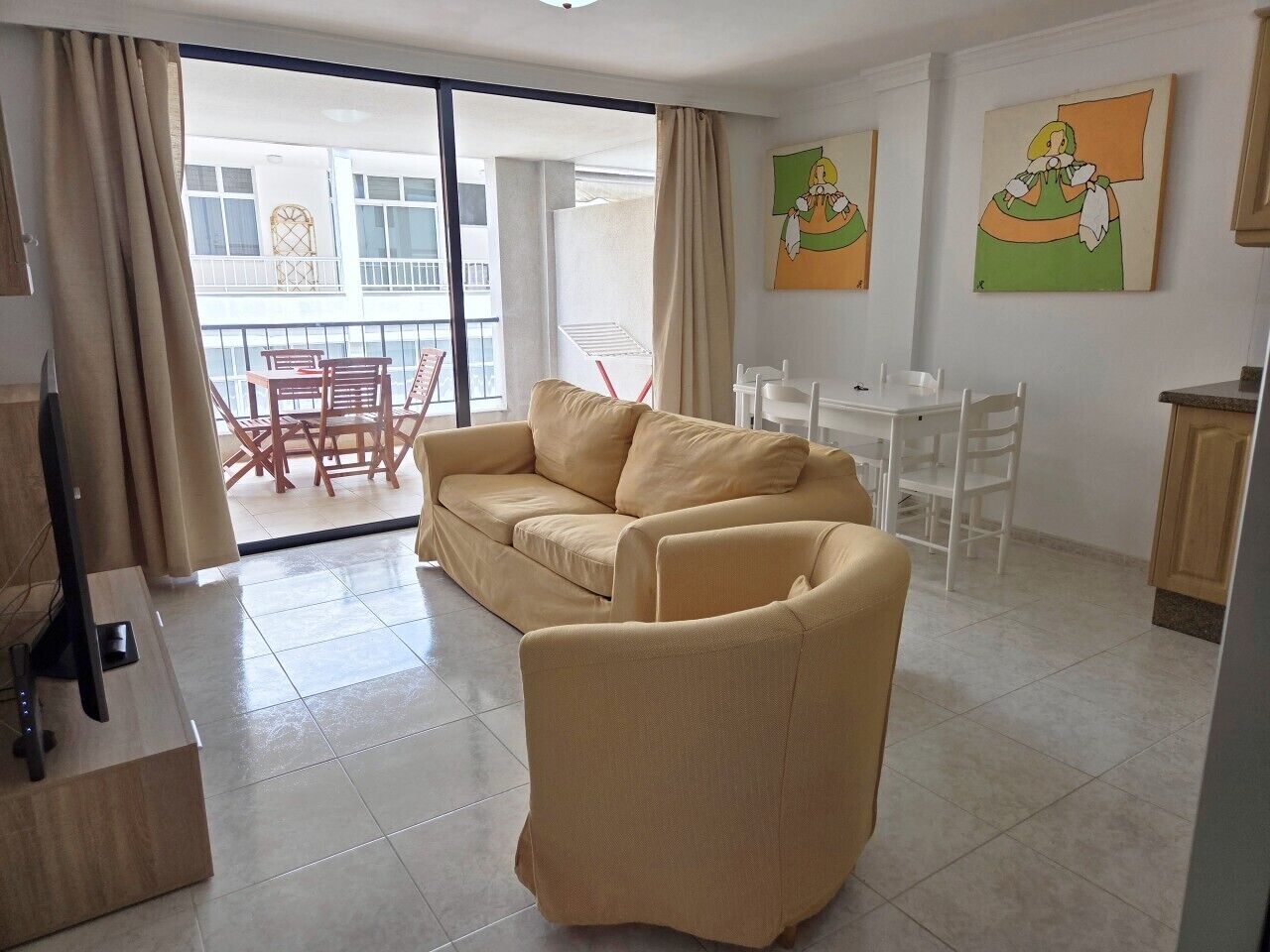 A living room with a sofa, a chair, a TV, and a balcony with a table and chairs.