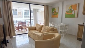 A living room with a sofa, a chair, a TV, and a balcony with a table and chairs. - Naos Costa Atlantica - Puerto Naos (Puerto Naos)