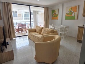 A living room with a sofa, a chair, a TV, and a balcony with a table and chairs.