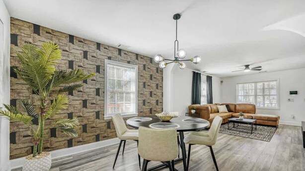 Ein modernes Wohnzimmer mit einem braunen Ledersofa, einem Esstisch mit Stühlen, einem Topf mit Pflanze und einer Wand mit Muster.