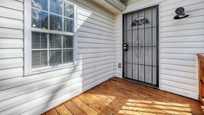 Eine Fassade aus weißem Holz mit einer Holzdachterrasse, einem Fenster mit Jalousien und einer schwarzen Metalttür mit dekorativem Design.