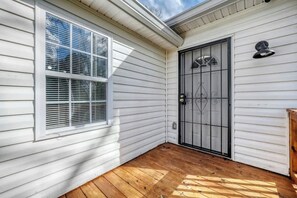 A white wooden exterior with a wooden deck, a window with blinds, and a black metal door with a decorative design. - Comfy Atlanta Retreat (Atlanta)