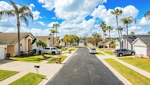 Una calle residencial con casas, coches aparcados y palmeras.