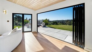 Ein modernes Interieur mit Holzboden, einem weißen Sofa und einer großen Schiebetür, die auf eine Terrasse im Freien führt.