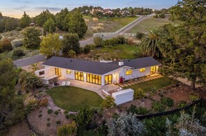 A modern house with a large patio, surrounded by a well-maintained garden and trees. - NEW! Arroyo Grande Wine Country Retreat.  Views, outdoor fireplace and barbecue. (Arroyo Grande)