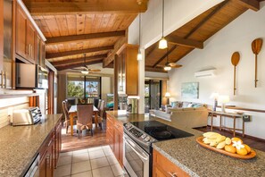 A spacious kitchen with granite countertops, wooden cabinets, and a large island. - Nihi Kai Villas 700 Ocean Views AC (Koloa)