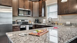 Una cocina moderna con armarios de madera oscura, electrodomésticos de acero inoxidable, encimera de granito y una isla central con alimentos.