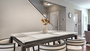 Un comedor con una mesa, sillas, un florero con flores y un reloj en la pared.