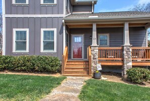 A two-story house with a front porch, a stone pillar, and a number '23' on the door. - Home Near Biltmore Estate | Pet-Friendly 3BR (30-Night Minimum + Year-Long Lease Option) (Asheville)