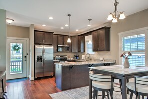 A modern kitchen with a central island, stainless steel appliances, pendant lighting, and a view of the outdoors. - Home Near Biltmore Estate | Pet-Friendly 3BR (30-Night Minimum + Year-Long Lease Option) (Asheville)