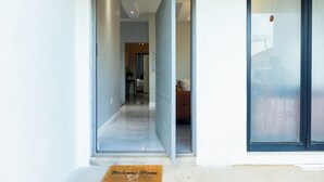 Una entrada moderna con puerta de cristal, felpudo y vista a una sala de estar con sofá y mesa de centro.