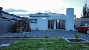 A modern house with a white exterior, a large circular outdoor seating area, and a red car parked in the driveway.