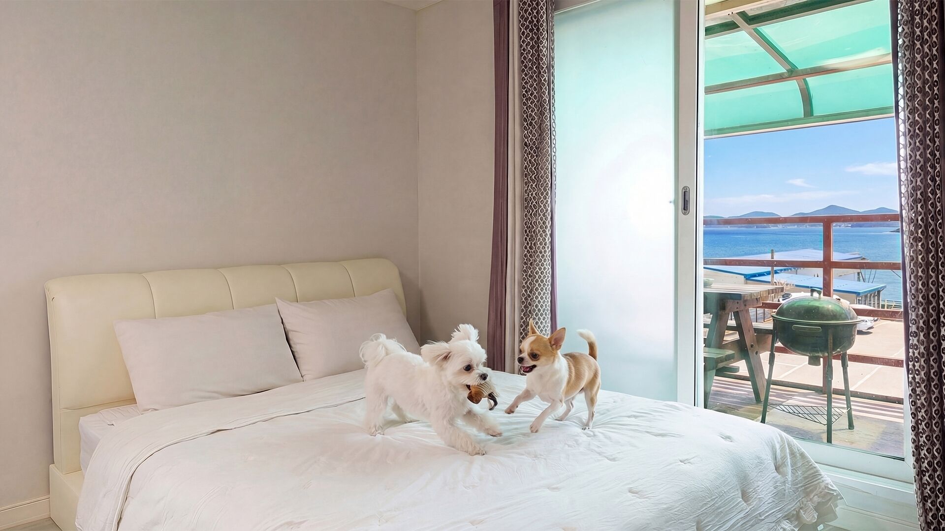 Ein Schlafzimmer mit Bett, zwei Hunden, Meerblick und einem Balkon mit Grill.