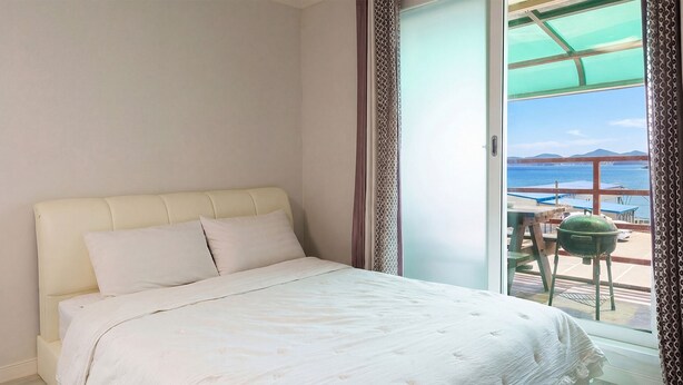 Een slaapkamer met een bed, uitzicht op zee en een balkon met buitenmeubilair.
