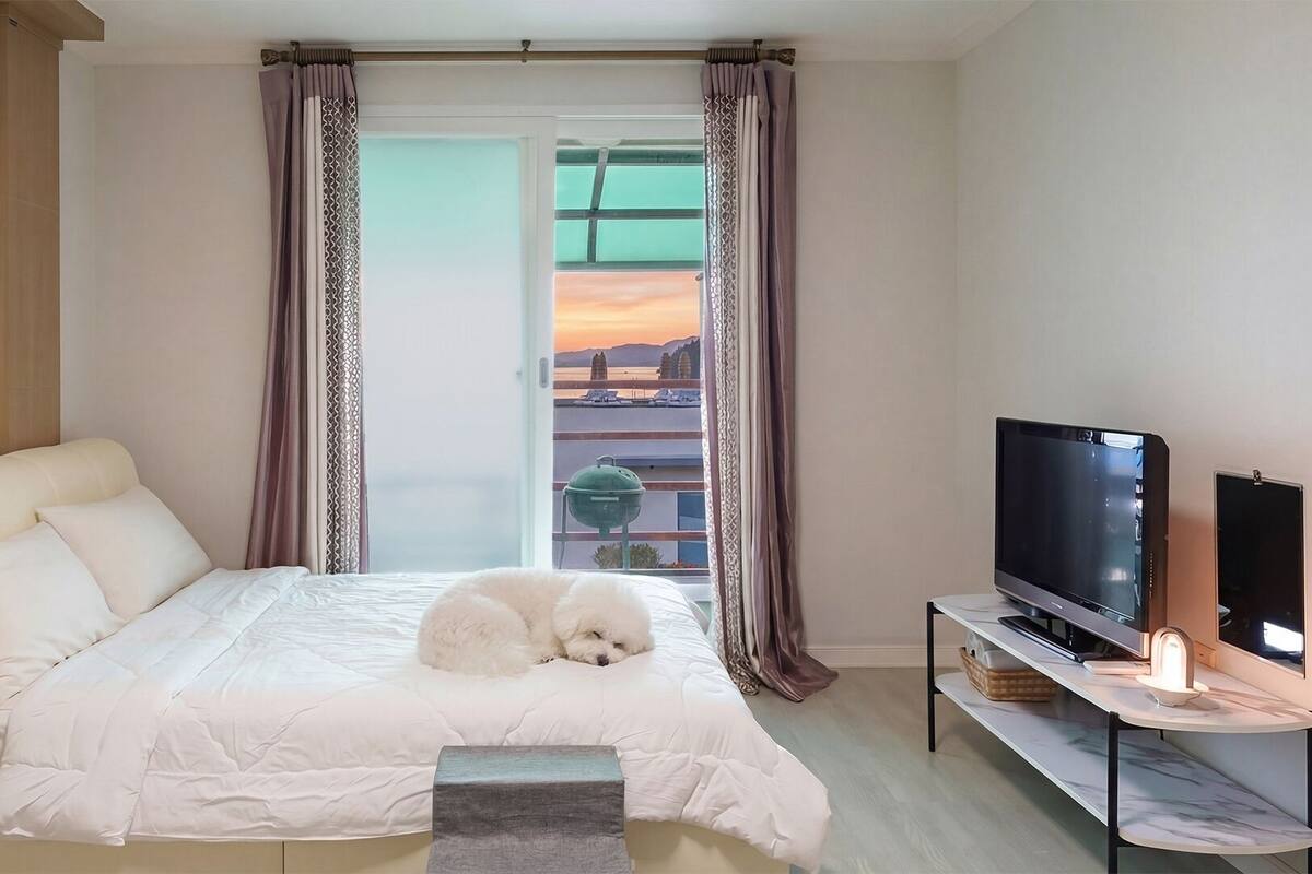 Een slaapkamer met een bed, een televisie en uitzicht op een zonsondergang door een raam.