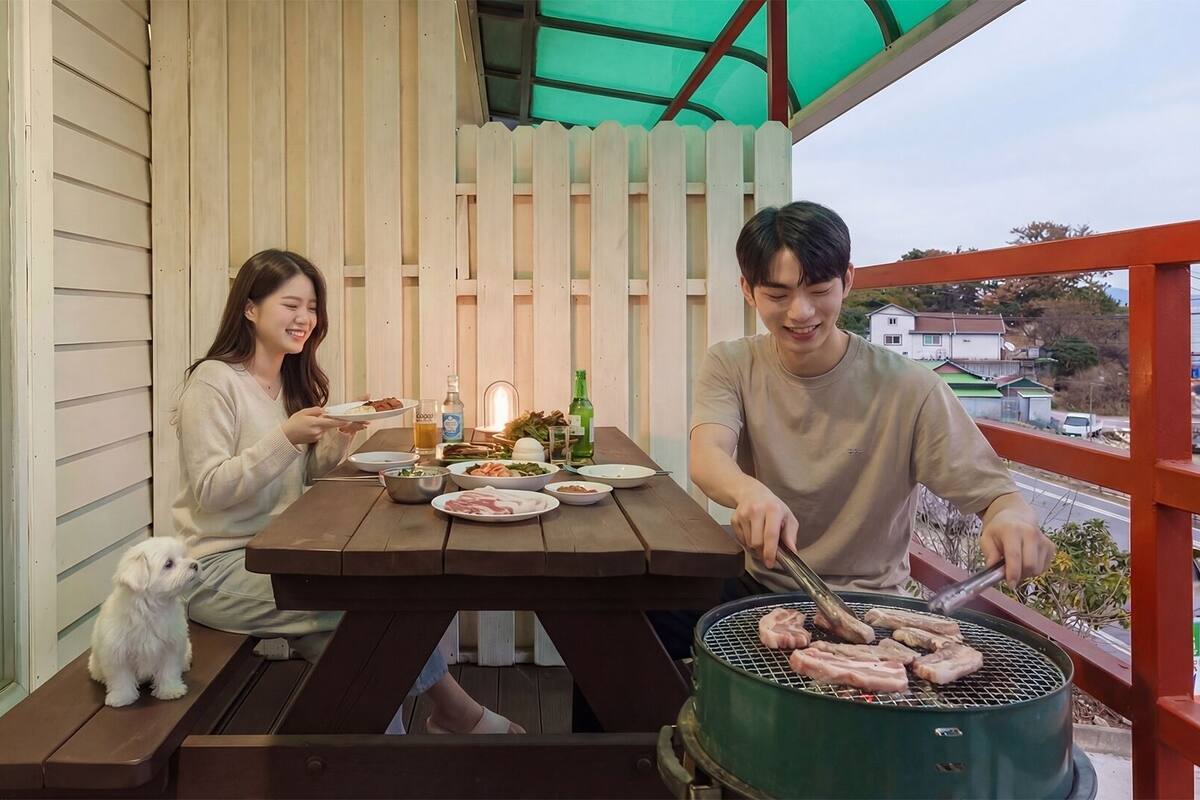Een houten terras met een picknicktafel, een barbecue en een kleine hond.