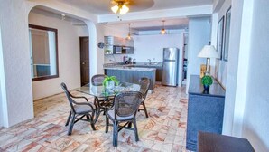 A dining area with a glass table and chairs, a kitchen in the background, and a ceiling fan. - Department Pino Amapas (Puerto Vallarta)