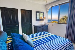 A bedroom with a large bed, two doors, a dresser, and a window with a view of the sea. - Department Pino Amapas (Puerto Vallarta)