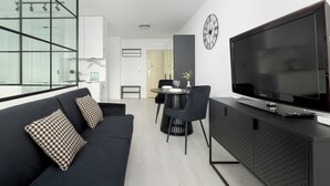 A modern living room with a black sofa, a dining area with a round table, and a large flat-screen TV on a black cabinet. - Szczecin Bronowicka Modern Apartment (Szczecin)