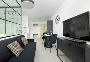 A modern living room with a black sofa, a dining area with a round table, and a large flat-screen TV on a black cabinet. - Szczecin Bronowicka Modern Apartment (Szczecin)