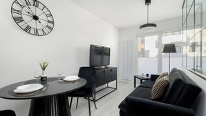 A modern living room with a dining area, featuring a large wall clock, a flat-screen TV, a sofa, and a dining table with chairs. - Szczecin Bronowicka Modern Apartment (Szczecin)