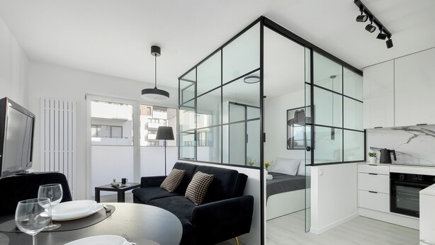 A modern apartment with a dining area, a black sofa, a kitchen, and a large glass partition. - Szczecin Bronowicka Modern Apartment (Szczecin)
