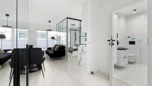 A modern interior with a dining area, black sofas, and a glass partition leading to a bathroom with a marble backsplash. - Szczecin Bronowicka Modern Apartment (Szczecin)