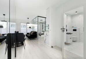 A modern interior with a dining area, black sofas, and a glass partition leading to a bathroom with a marble backsplash. - Szczecin Bronowicka Modern Apartment (Szczecin)