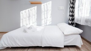 A neatly made bed with white linens and a rolled towel, a wooden floor, and a window with sheer curtains allowing natural light. - Park nad Jasieniem Studio (Łódź)