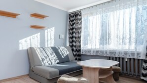 A modern living room with a grey sofa, a round wooden coffee table, and a patterned throw pillow. - Park nad Jasieniem Studio (Łódź)