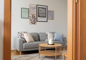Ein modernes Wohnzimmer mit einem grauen Sofa, einem runden Holztisch und drei gerahmten Kunstwerken an der Wand.