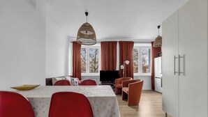 Ein Essbereich mit einem Tisch für vier Personen, roten Stühlen, einem Fernseher und einem großen Fenster mit Vorhängen.
