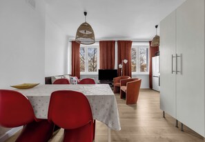 A dining area with a table set for four, red chairs, a television, and a large window with curtains. - Ochota Kopińska Homely Apartment (Warszawa)