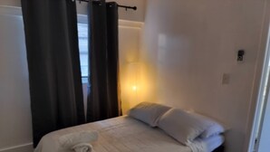 Et soveværelse med seng, gardiner, et natbord og en lampe.