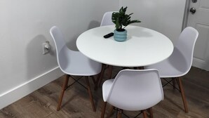 Et spiseområde med et rundt hvidt bord, fire hvide stole, en potteplante og tre spejle på væggen.