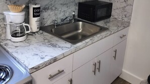 Et moderne køkken med hvide skabe, en marmor bordplade, kaffemaskine, mikroovn og gasblus.