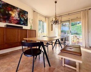 A dining area with a wooden table, black chairs, a bench, a chandelier, and a large abstract painting on the wall. - Calma Mar by Costabravaway (Sant Feliu de Guíxols)