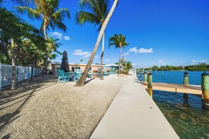 A beachside area with palm trees, a concrete walkway, and a dock extending into the water. - Casa de Rosa - Key Colony Beach Waterfront Pool Home (Key Colony Beach)