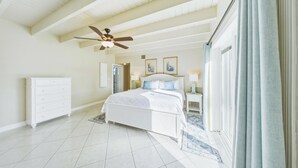 Une chambre avec un grand lit, un ventilateur de plafond, une commode et une vue sur l’extérieur.