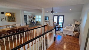 A spacious living area with a wooden dining table, a white sofa, and a staircase with a white railing. - Family-Friendly 5BR Lake Hartwell Lakefront Getaway with Dock ~ Sunset Shores (Martin)