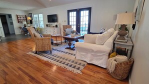 A spacious living room with hardwood flooring, a white sofa, wicker chairs, a coffee table, and a TV. - Family-Friendly 5BR Lake Hartwell Lakefront Getaway with Dock ~ Sunset Shores (Martin)