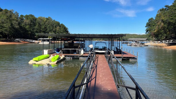 A dock with a covered seating area, a green inflatable boat, and a calm lake. - Family-Friendly 5BR Lake Hartwell Lakefront Getaway with Dock ~ Sunset Shores (Martin)