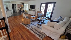 A spacious living area with a wooden floor, a white sofa, wicker chairs, a dining table, and a kitchen in the background. - Family-Friendly 5BR Lake Hartwell Lakefront Getaway with Dock ~ Sunset Shores (Martin)