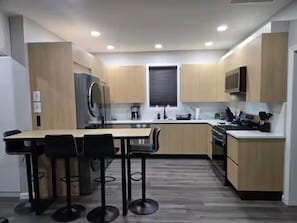 Une cuisine moderne avec des meubles en bois, un îlot central doté de tabourets de bar et des appareils électroménagers intégrés.